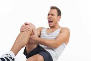 Man, wearing athletic clothes, yells out and grabs his knee after a patellar dislocation while playing basketball