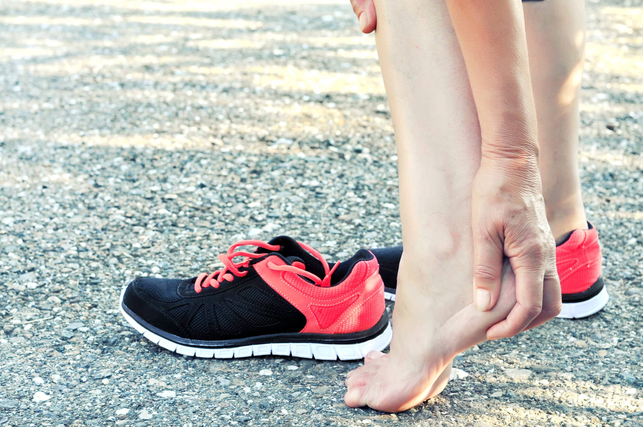 Athlete clutching their painful heel, with a black and red tennis shoe nearby
